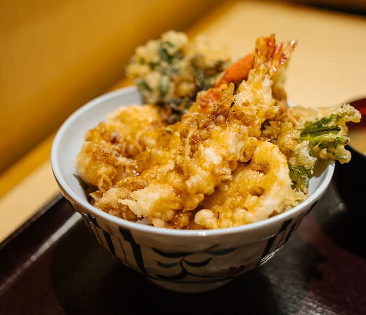 Tempura served in a bowl, on a brown tray, alongside dipping sauces.
