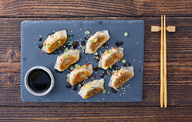 Dumplings served with soy sauce, on black tray with chopsticks.